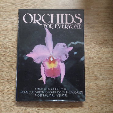 Book titled 'Orchids for Everyone' with a pink orchid on the cover, placed on a wooden surface.