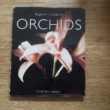 Book titled 'Beginner's Guide to Orchids' by Geoffrey Hands on a wooden surface
